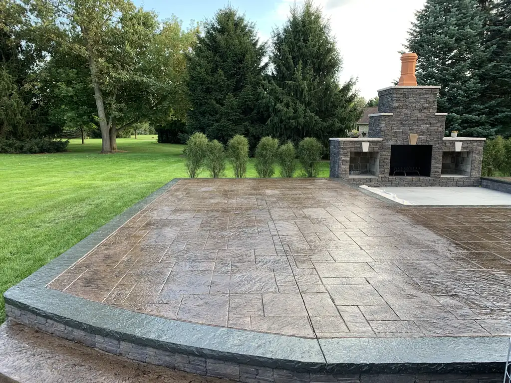 Large stamped concrete patio with a stone outdoor fireplace